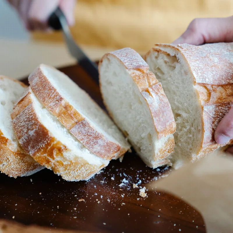 Hands slice a golden-brown loaf to reveal a soft, pale crumb