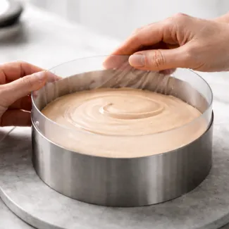 Roka poravnava nagubano acetatno folijo v tortnem obroču z mousse maso za popoln gladek rob