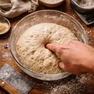Roka pritiska prst v mehko, zračno testo za kruh, v domači kuhinji z rahlo moko okoli